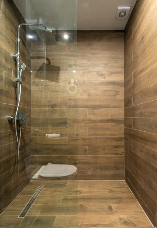 Ducha a ras de suelo con revestimiento tipo madera y mampara de cristal