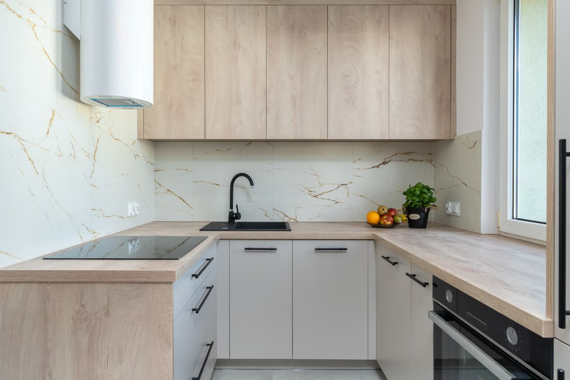 Cocina reformada en madera clara con frente de mármol y ventana
