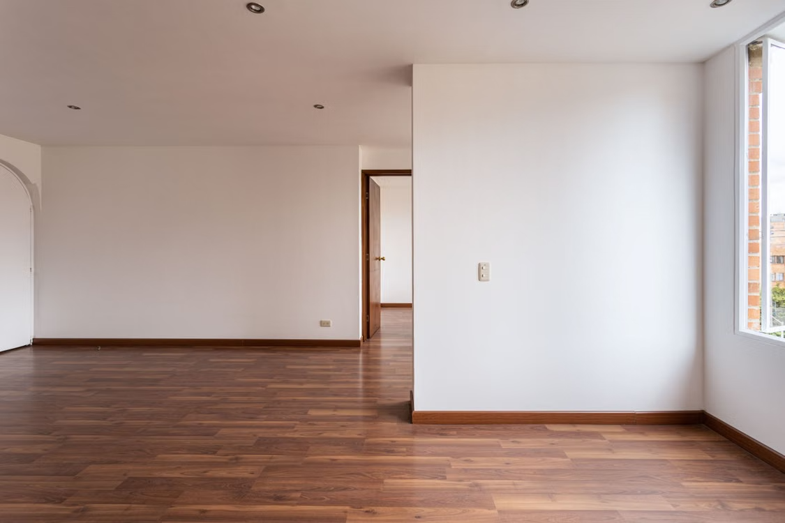 Salón reformado con suelo de madera, paredes blancas y luz natural
